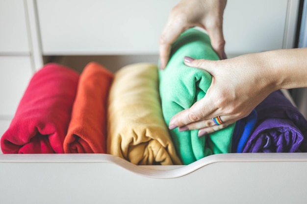 A close-up shot of a woman's hands selecting brightly colored clothes from a neatly organized closet. The clothes range from vibrant pinks and yellows to calming blues and greens, emphasizing the variety of colors used in dopamine dressing.