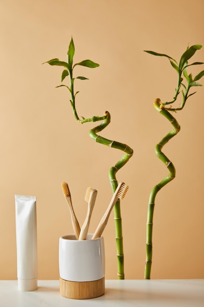 A brightly lit bathroom scene showcasing a bamboo toothbrush in a minimalist holder next to a small glass container of toothpaste tablets. The background includes a blurred view of a white sink and a neatly folded reusable cloth. This suggests a clean, eco-conscious dental hygiene routine aimed at reducing plastic waste.