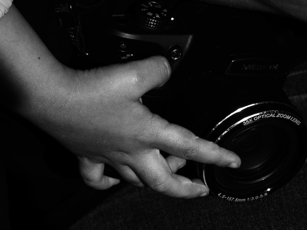 A pair of hands holding a developed 35mm film negative up to the light, examining the images. The background is blurred, but shows a dimly lit room with vintage photography equipment.