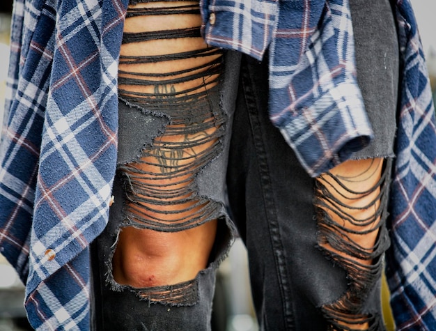 A person wearing an oversized flannel shirt over a vintage band t-shirt, paired with ripped black jeans and Dr. Martens boots, standing in front of a brick wall with graffiti, showcasing the edgy and rebellious spirit of the grunge comeback.