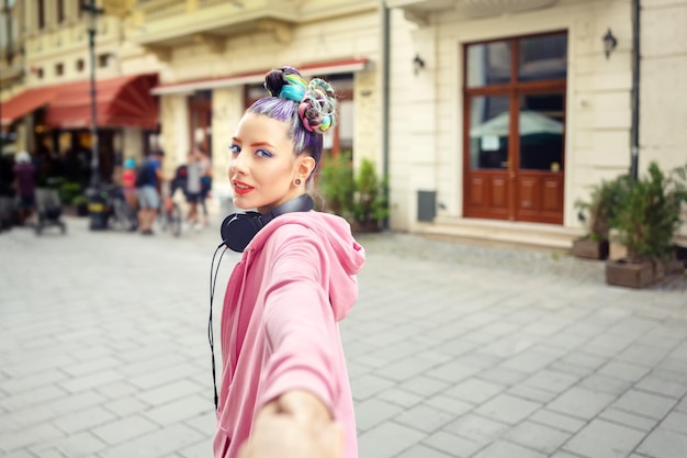 A street style photo showing a young woman with a messy bun secured with a large, brightly colored velvet scrunchie. She is wearing a casual yet stylish outfit consisting of a vintage band t-shirt, high-waisted jeans, and sneakers, showcasing how the scrunchie complements her overall look.