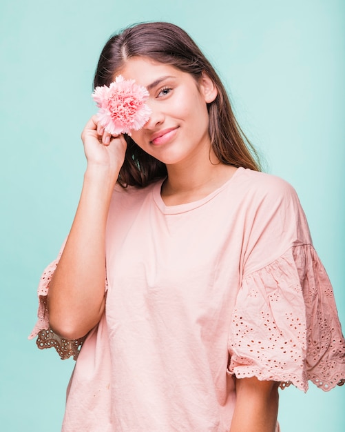 A close-up shot of a young woman wearing a pastel pink baby tee with a graphic butterfly print, paired with high-waisted light wash jeans and chunky white sneakers. She is holding a translucent pink baguette bag and smiling confidently. The background is a blurred pastel-colored wall.
