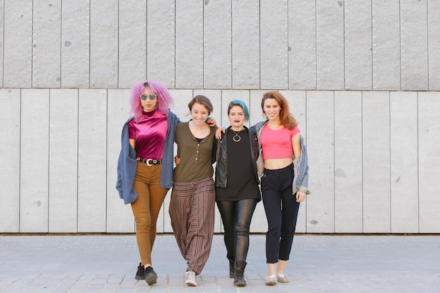 A group of teenagers in the early 2000s showcasing classic emo fashion. They are wearing black skinny jeans, band t-shirts, studded belts, and Converse sneakers. Their hair is styled with side-swept bangs and some have dyed their hair black or with bright streaks. They are standing together, looking angsty, and holding skateboards.