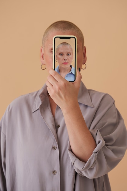 A person looking at their reflection in a phone screen showing a reverse aging filter, with a visible expression of concern and dissatisfaction in their eyes. The background is a dimly lit room, emphasizing the introspective and potentially negative emotions.