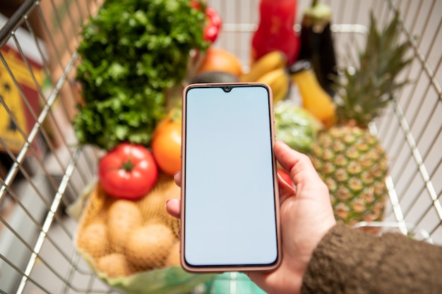 A close-up shot of a smartphone screen displaying an online grocery shopping app. The screen shows various fresh produce items, alongside a banner highlighting the 20% cashback promotion. The image emphasizes the ease and convenience of selecting groceries online.