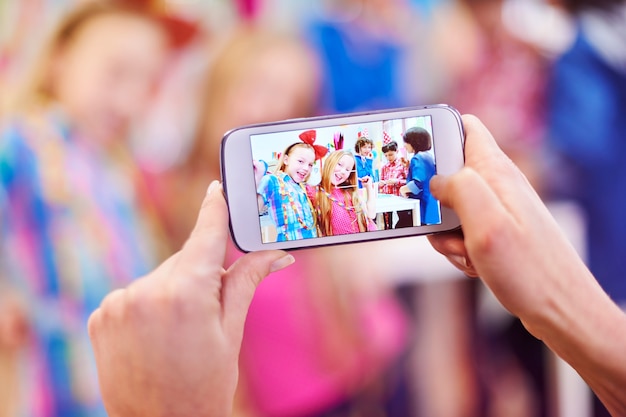 A brightly lit smartphone screen displaying a TikTok video of a group of people performing a synchronized dance routine. The video is overlaid with text promoting a dance challenge and a brand logo. The background is blurred, suggesting the phone is being held by someone watching the video.