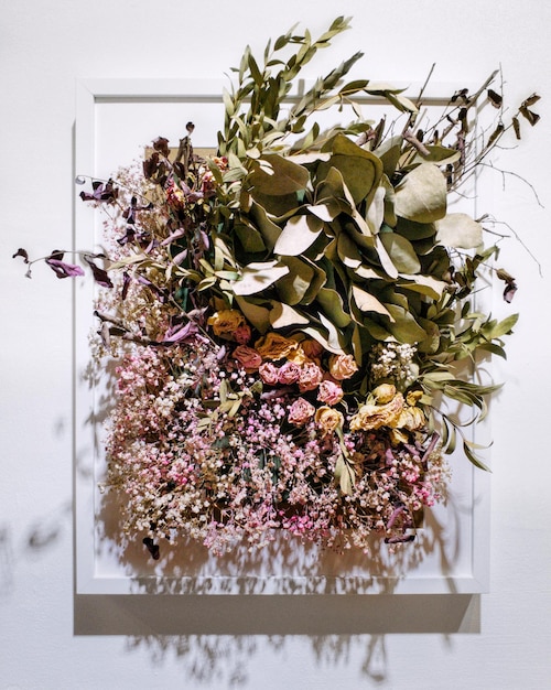 Close-up shot of a finished pressed flower wall art piece, featuring delicate wildflowers carefully arranged and pressed between two sheets of glass in a simple wooden frame. The background shows a soft, diffused natural light coming through a window.