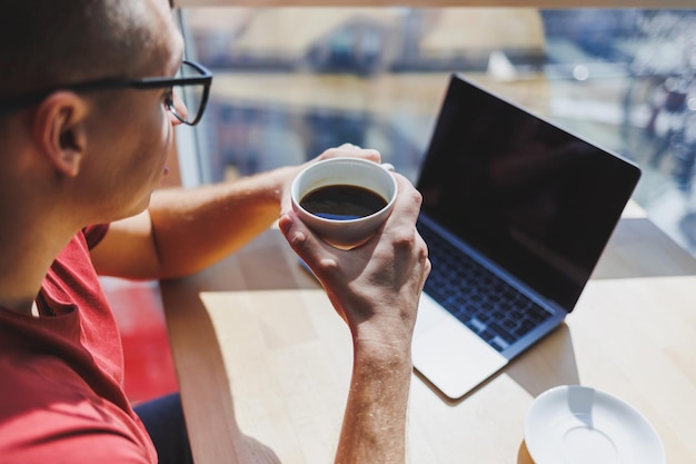 An eye-level shot of a person using a laptop in a coffee shop, browsing an online marketplace for deals on refurbished electronics. The screen shows product listings with discounted prices and customer reviews.